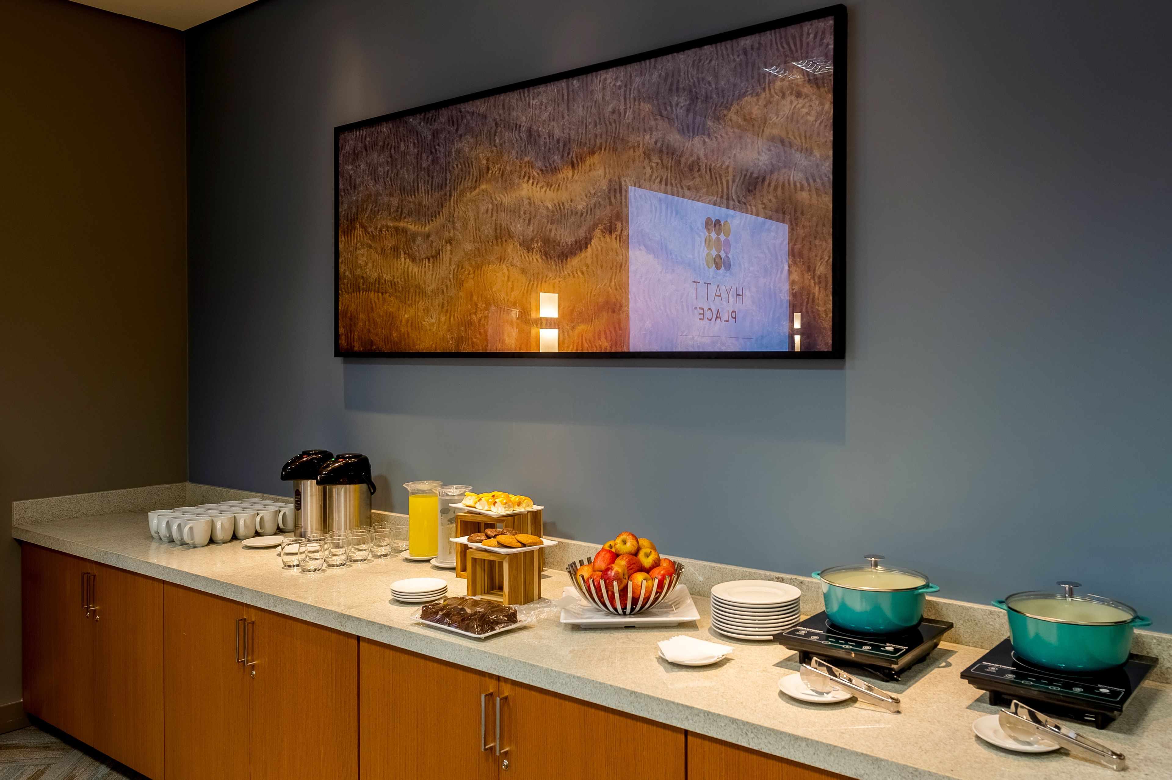 Disposição de buffet de café da manhã com diversos alimentos, uma máquina de café e uma pintura grande na parede.