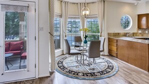 Een moderne keuken met een groot eiland, een eethoek met een ronde tafel en stoelen, en een stadszicht door grote ramen.