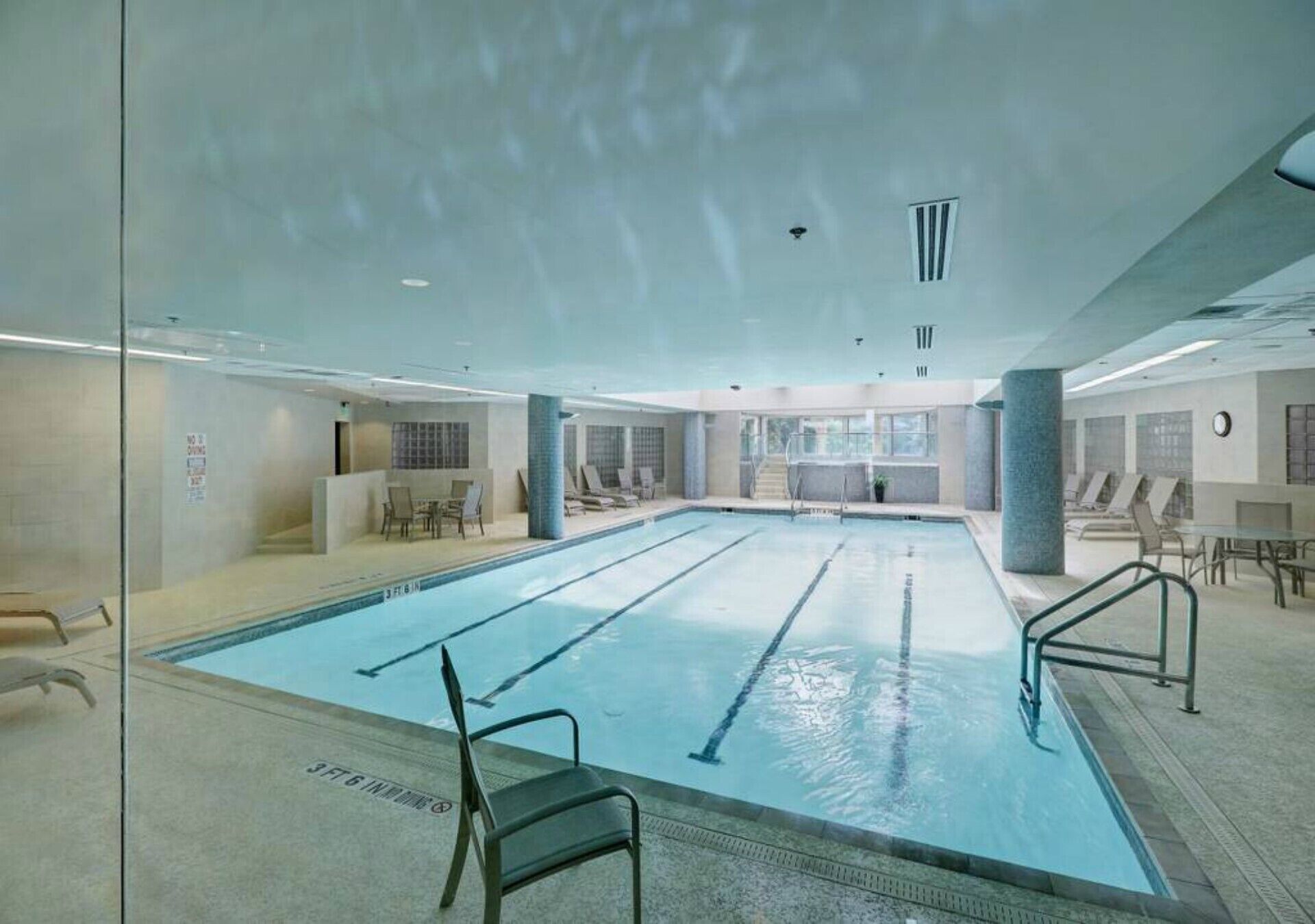A large indoor swimming pool with clear lanes, lounge chairs, and a glass wall on one side.