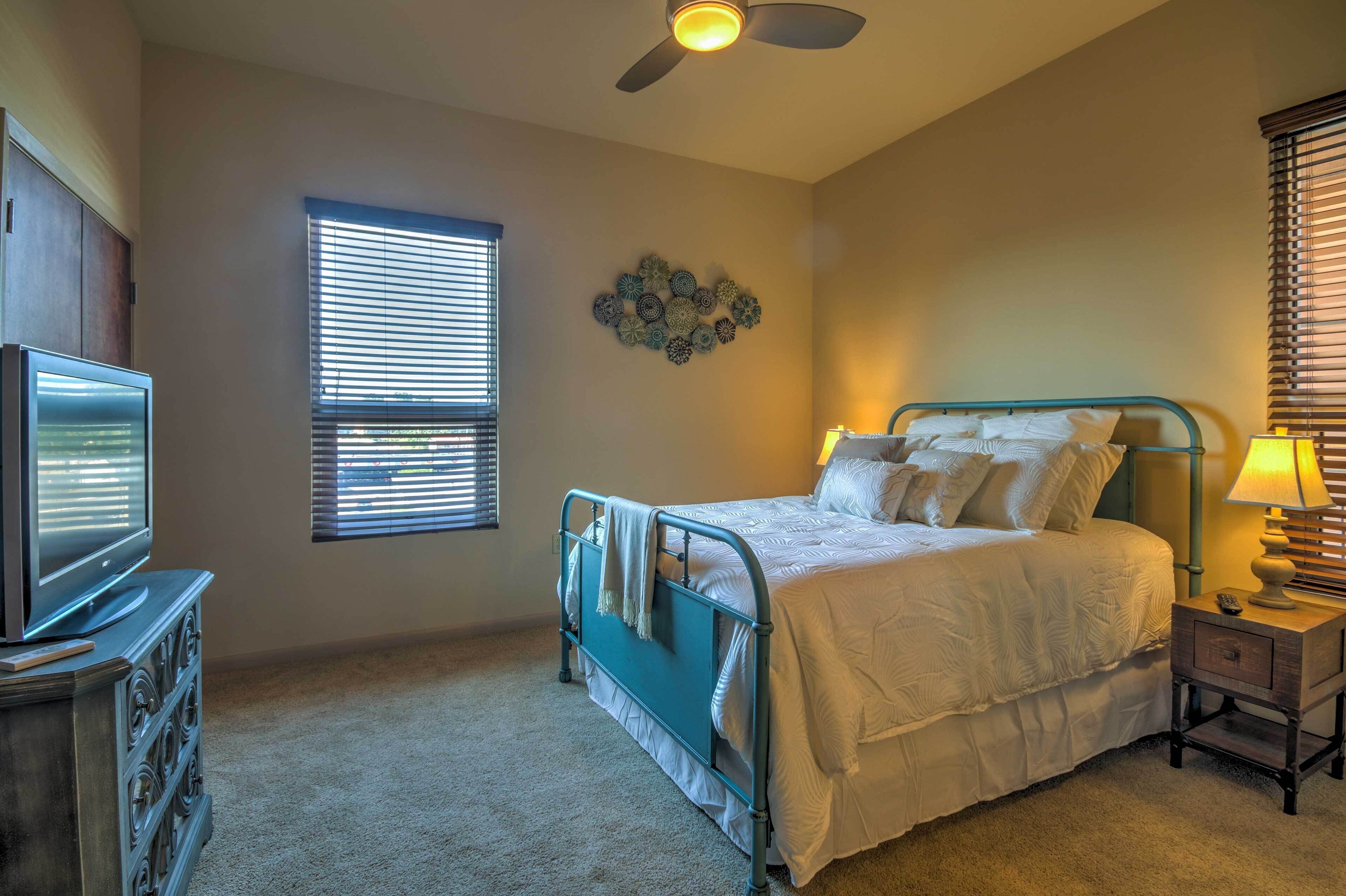 A bedroom with a bed, a TV, a ceiling fan, and a window with blinds.
