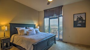 A bedroom with a large bed, a nightstand, a window with blinds, and a poster on the wall.