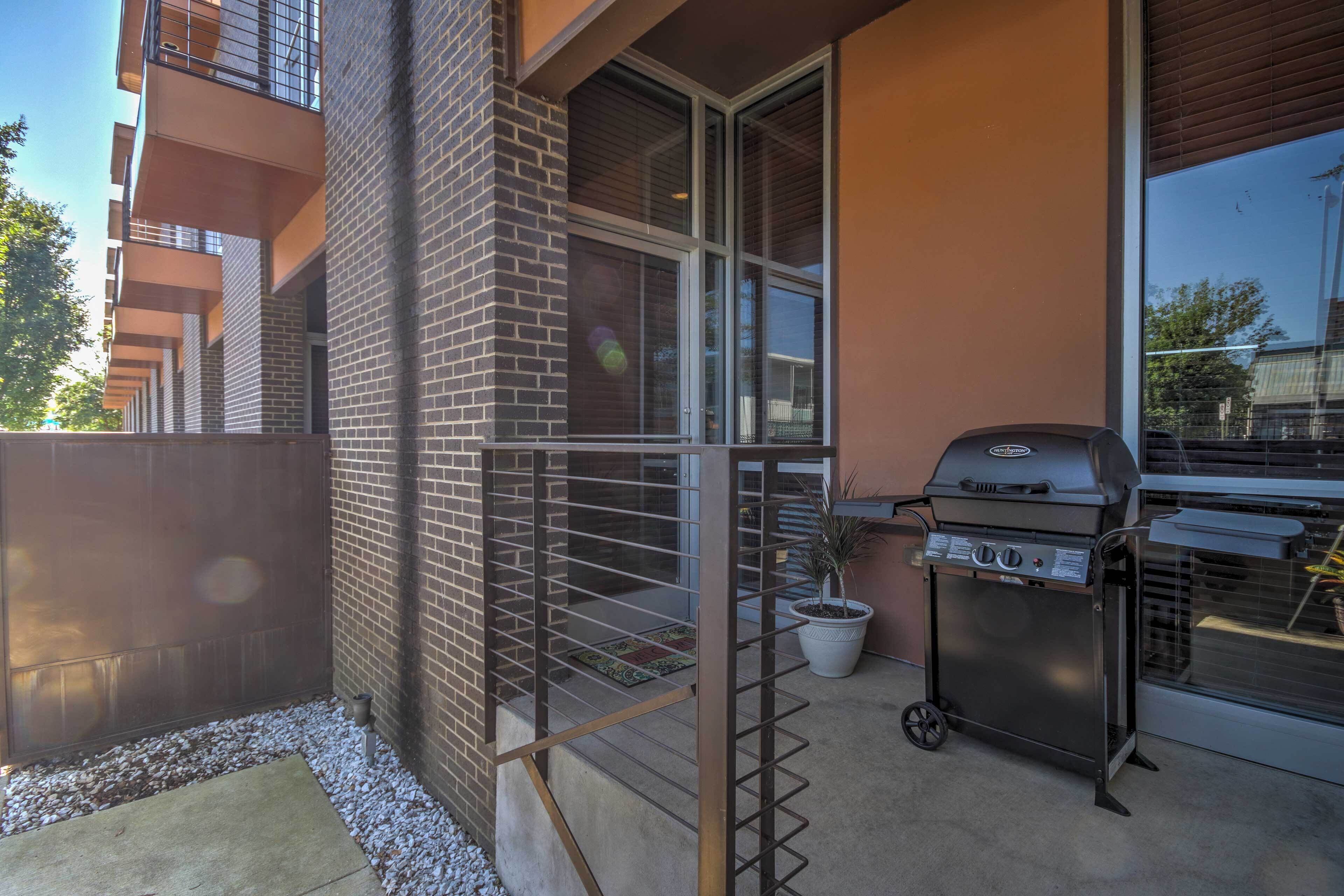 A balcony with a grill, a potted plant, and a view of a neighboring building.