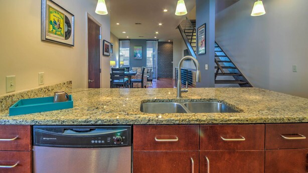 A kitchen with granite countertops, stainless steel appliances, and a dishwasher. There is a staircase leading to a dining area with a view of the outdoors.