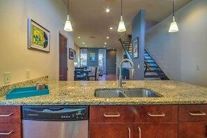 A kitchen with granite countertops, stainless steel appliances, and a dishwasher. There is a staircase leading to a dining area with a view of the outdoors.