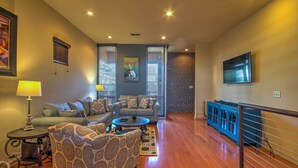 A living room with a sofa, armchair, coffee table, and a TV mounted on the wall.