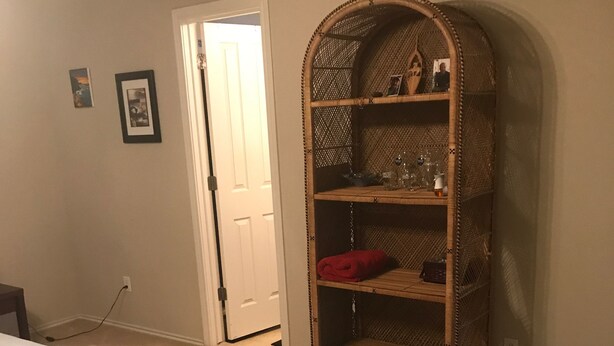 A bedroom with a bed, a large wicker shelving unit, and a door leading to another room. - Wonderful home (4 bdr, 3 bth) cozy! (Cibolo)