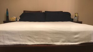 A neatly made bed with a white comforter and dark pillows, a bedside table with a lamp, a tissue box, and a water bottle. - Wonderful home (4 bdr, 3 bth) cozy! (Cibolo)