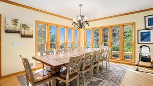 A dining area with a wooden table and chairs, large windows, and a chandelier. - Luxury 7BR multifamily on Lake Michigan, Pool & Spa, New Kitchen and Lake Porch! (South Haven)