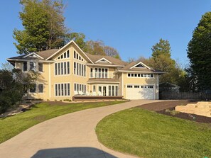 Une maison à deux étages avec un grand garage, un porche avant couvert et une allée menant à l’entrée.
