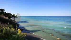 A coastal landscape with clear blue water, a sandy beach, and dense greenery. - Luxury 7BR multifamily on Lake Michigan, Pool & Spa, New Kitchen and Lake Porch! (South Haven)