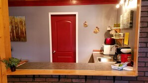 A kitchen with a red door, a wooden ceiling, and three blue stools. - Mooseberry Cabin (Tok)