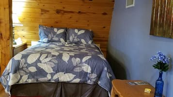 A wooden-paneled room with a bed, a small table, and a vase with flowers.