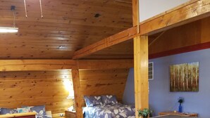 A cozy room with a sofa, a small table, a bed with floral bedding, and a blue wall with a painting. - Mooseberry Cabin (Tok)