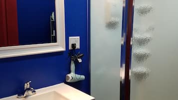 A bathroom with a blue wall, a white sink, a mirror, a towel rack, and a glass shower enclosure.