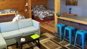 A cozy room with a sofa, a small table, and a kitchen area with stools. - Mooseberry Cabin (Tok)