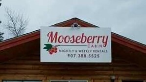 A wooden building with a sign that reads "Mooseberry" and a phone number. - Mooseberry Cabin (Tok)
