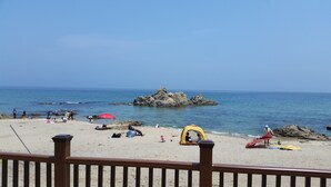 Ein Strand mit Menschen, Zelten und einem Felsen im Wasser.