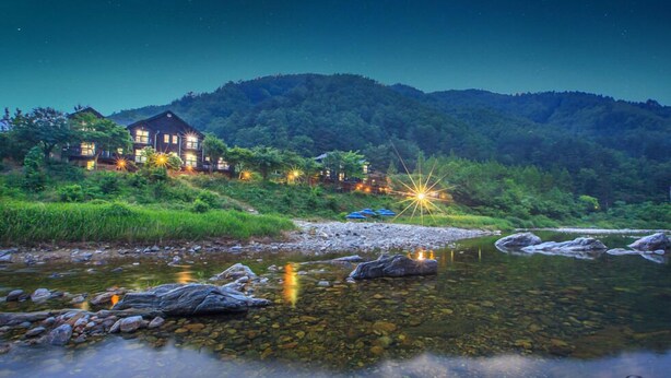 Ein Fluss-Hotel mit klarem Wasser, Felsen und einer Bergkulisse.