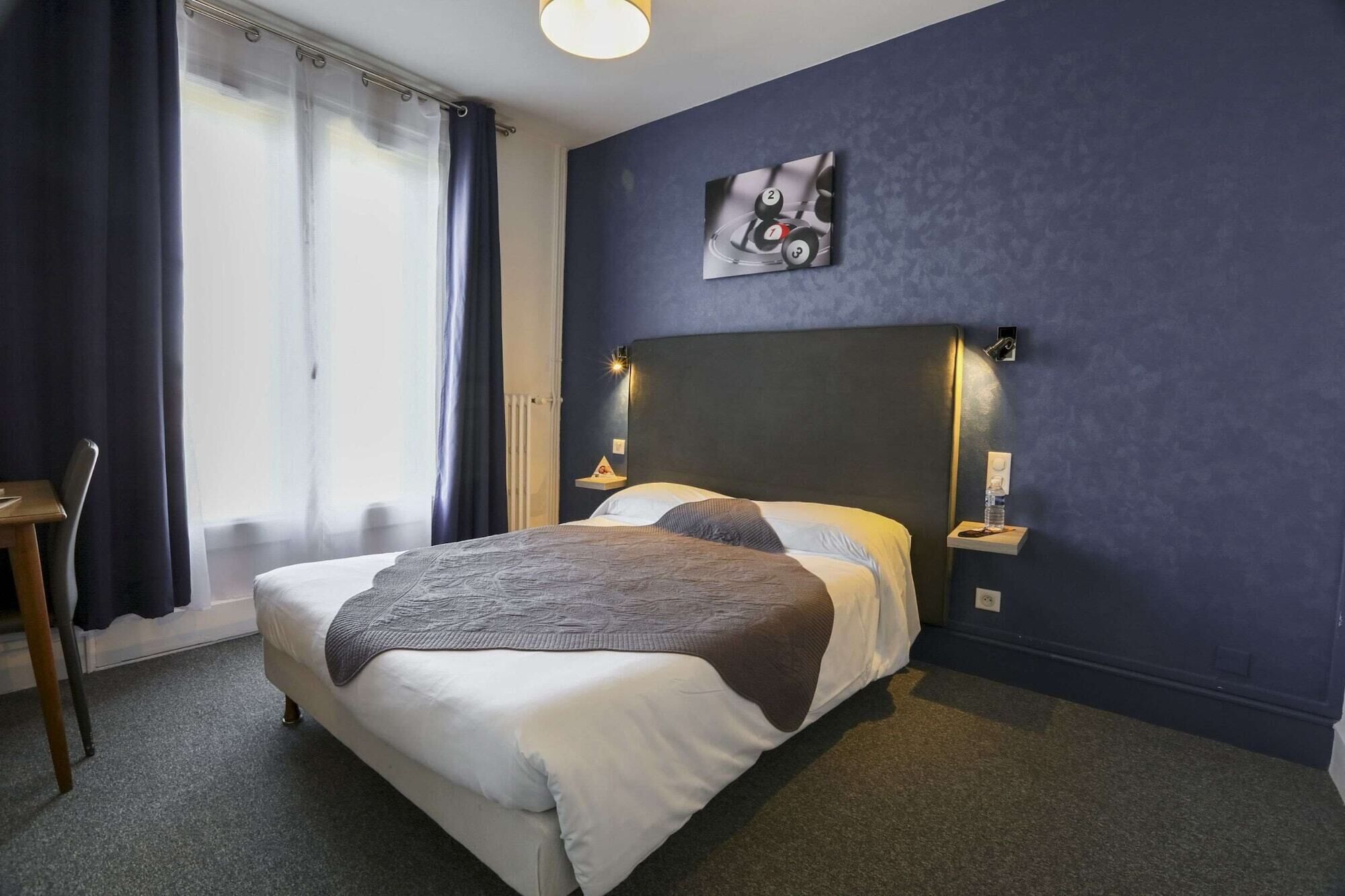 Habitación de hotel con cama, sillón, mesita de noche y lámpara fijada a la pared.