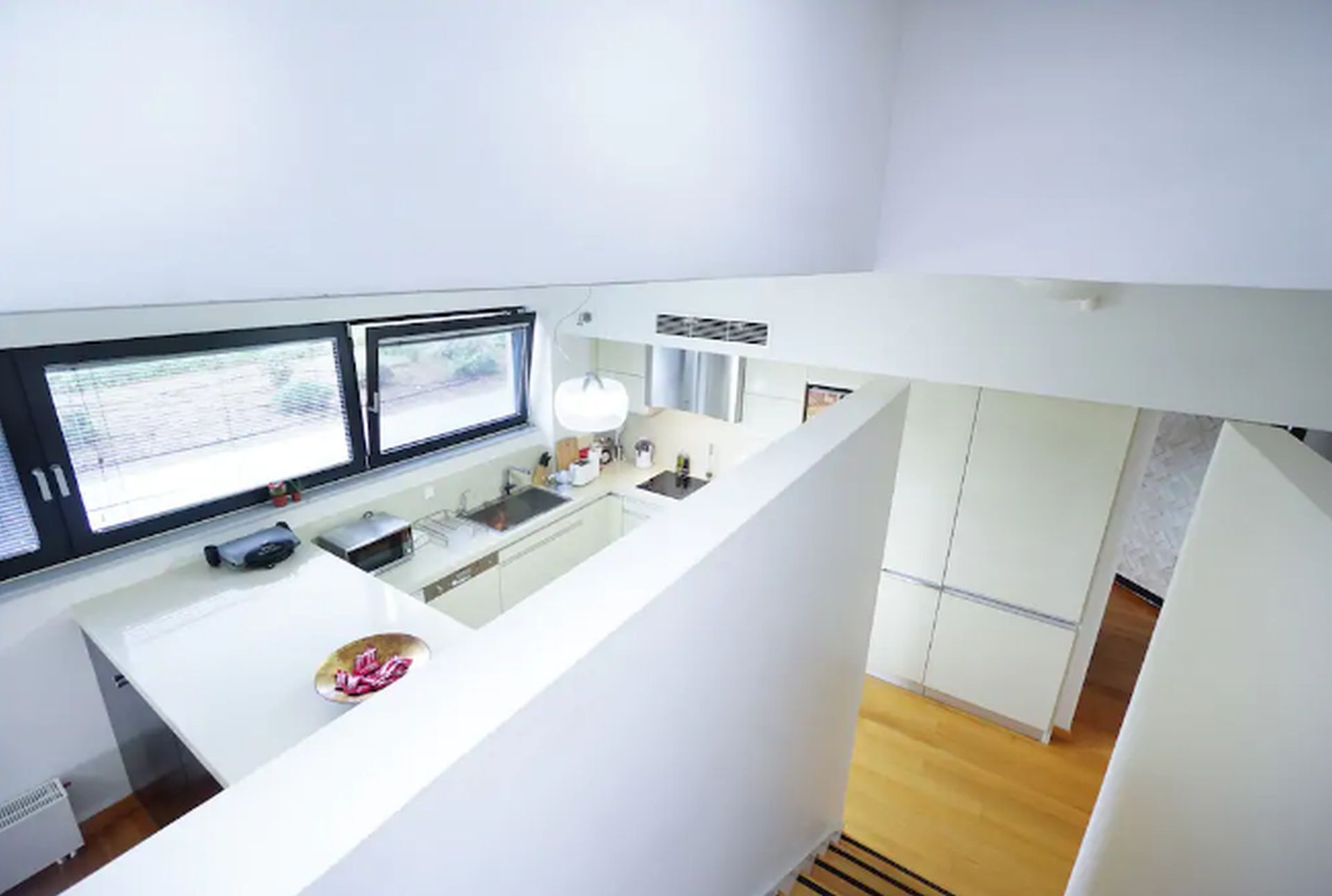A modern kitchen with a white countertop, two monitors, and a sink.