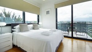 Una habitación de hotel moderna con una cama grande, una mesita de noche, una silla y un balcón con vistas a la ciudad.