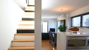 Una cocina moderna con horno empotrado, un comedor con sillas y una escalera con escalones de madera.