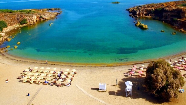 Una playa con aguas turquesas cristalinas, orilla de arena y numerosas sombrillas.