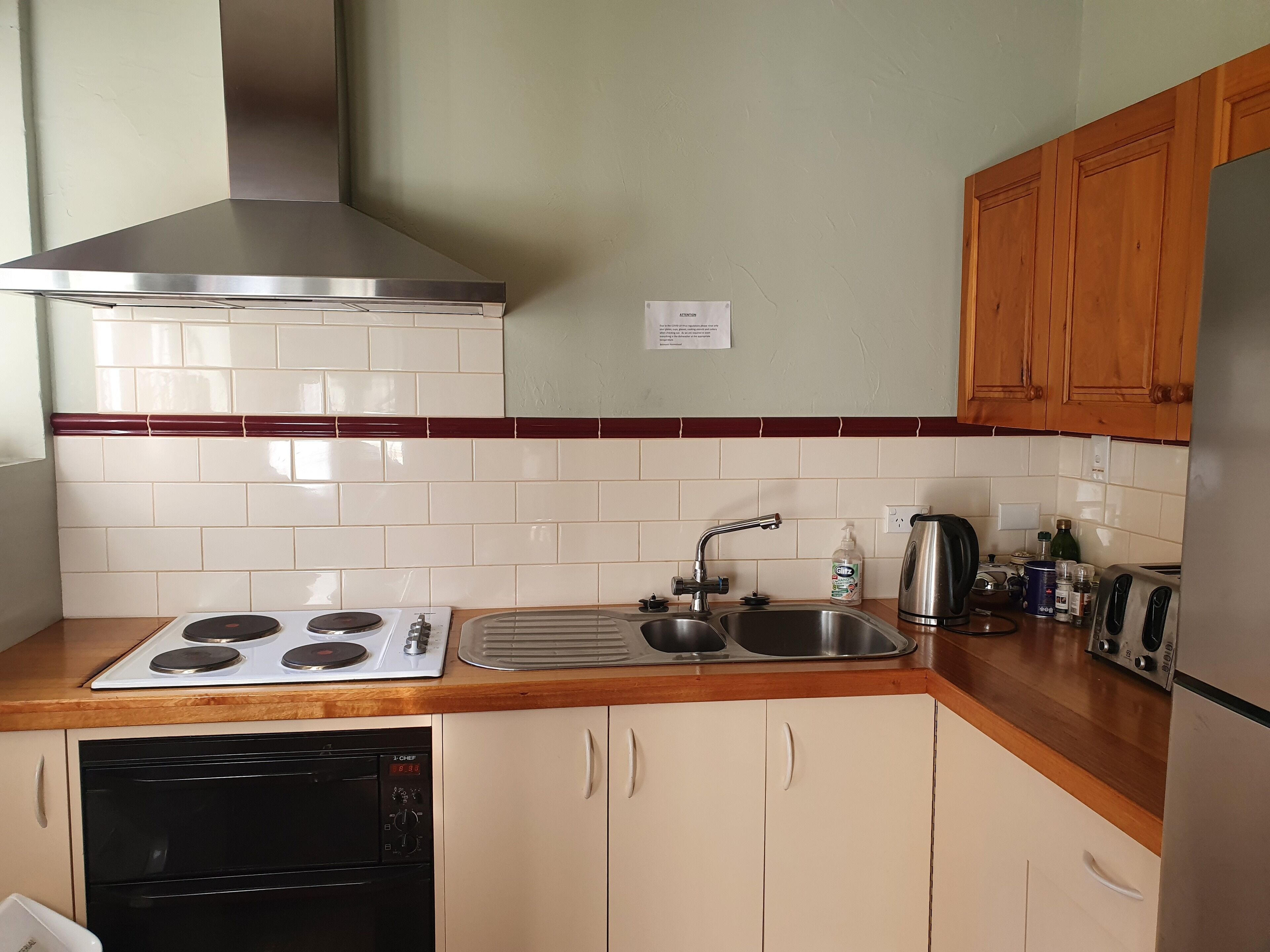 Cocina equipada con estufa, lavaplatos y lavadero, armarios de madera y extractor de acero inoxidable.