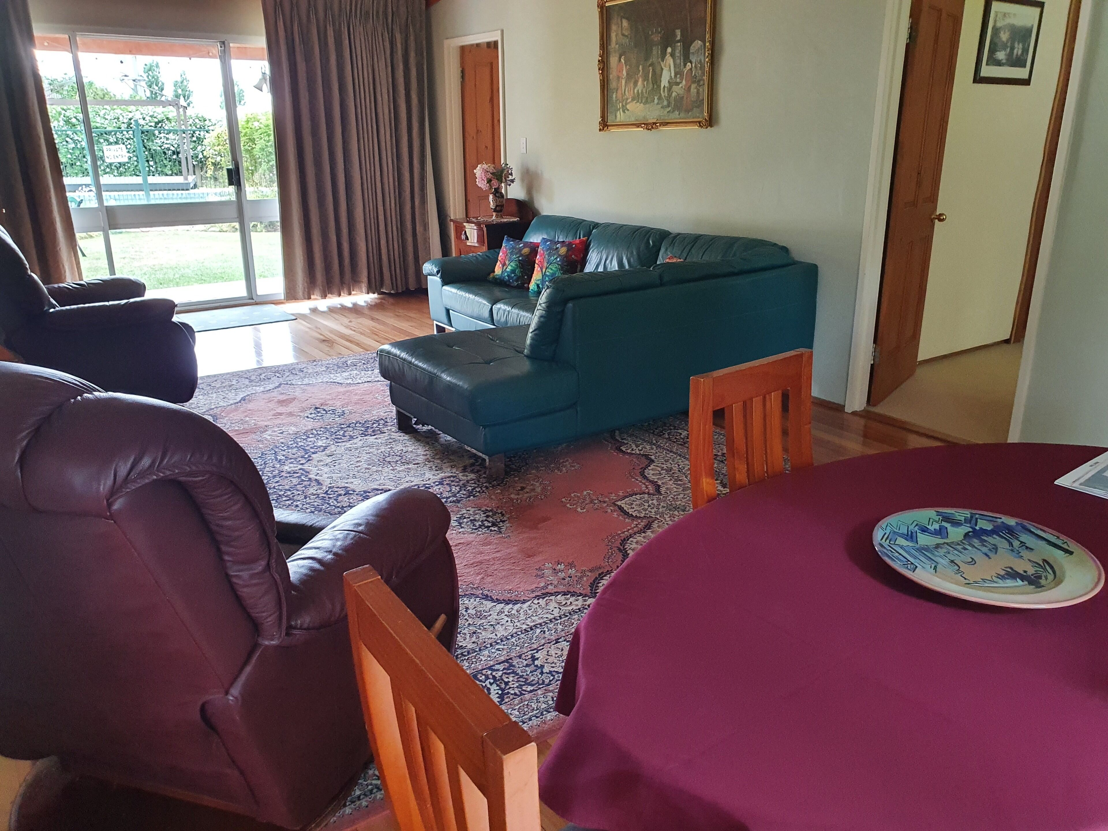 A living room with a blue sofa, a wooden chair, a table with a red tablecloth, and a patterned rug.