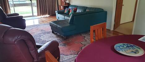 A living room with a blue sofa, a wooden chair, a table with a red tablecloth, and a patterned rug.
