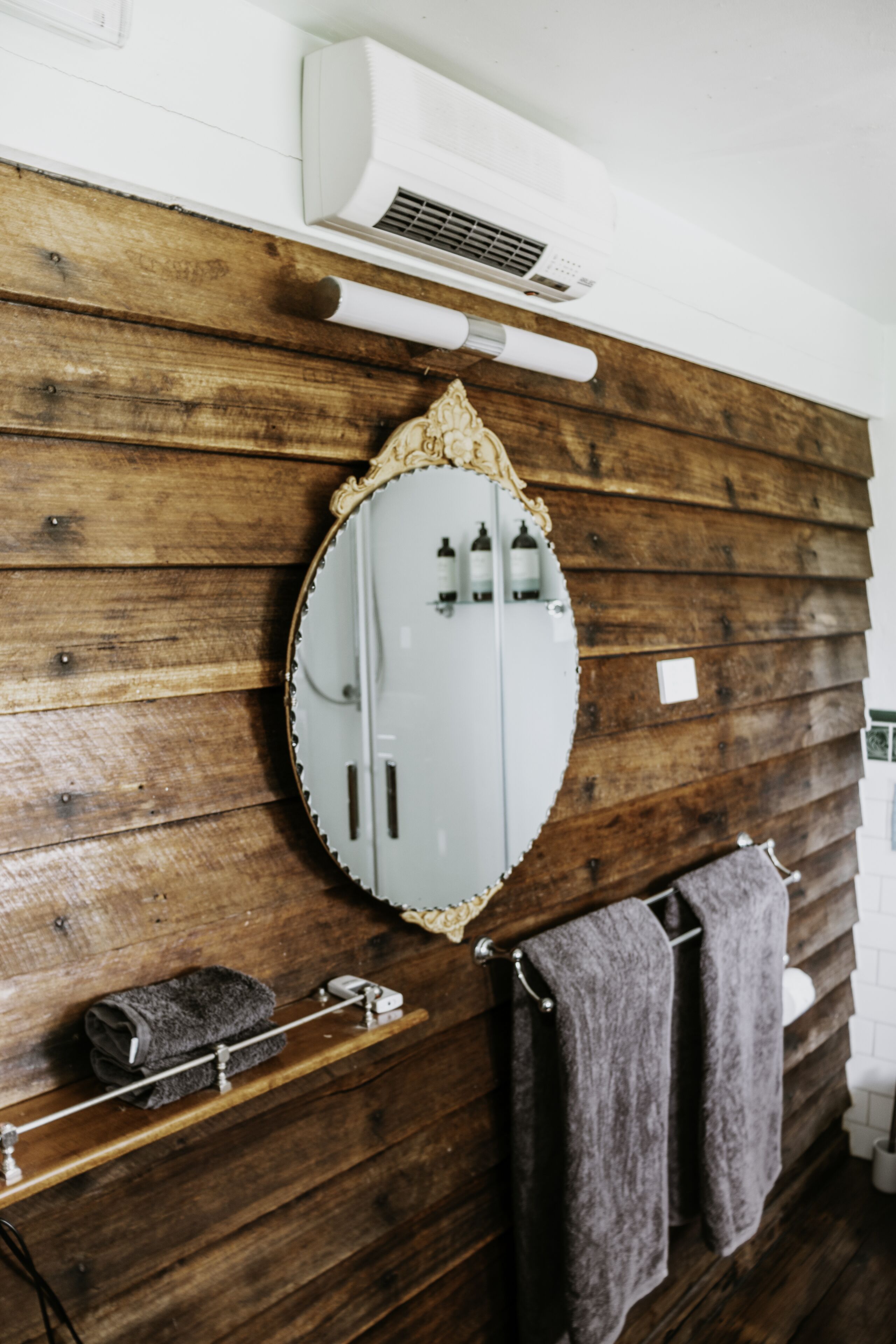 A bathroom with a wooden wall, a white vanity, a mirror, and a towel rack.