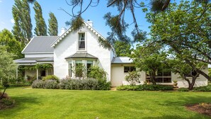 A white house with a gabled roof, surrounded by a well-maintained lawn and various shrubs. - Belmont Homestead (Swansea)