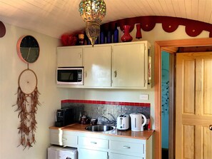 A compact kitchen with white cabinets, a microwave, a sink, and a coffee maker.
