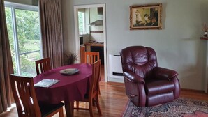 A dining area with a table set for two, a leather armchair, and a painting on the wall. - Belmont Homestead (Swansea)