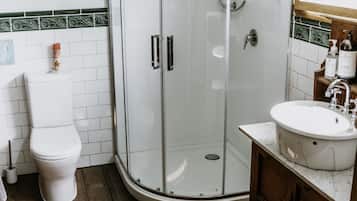 A corner bathroom with a glass-enclosed shower, a toilet, and a sink with a wooden vanity.