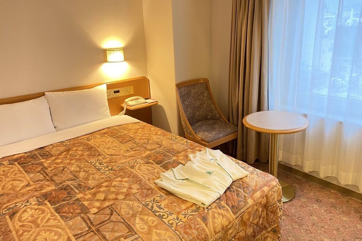 A hotel room with a large bed, a chair, a small table, a phone, and a window with curtains.
