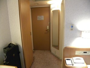 Une chambre d’hôtel avec une porte, un miroir, une table de chevet avec un téléphone et un petit radiateur.