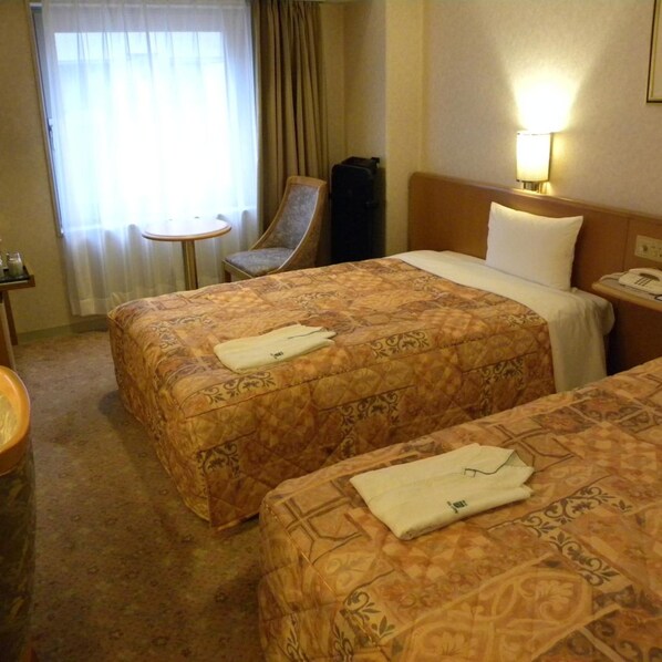 Une chambre d’hôtel avec deux lits, une chaise, une petite table et une lampe.