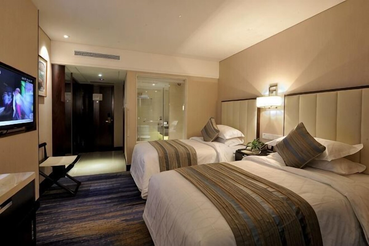 Quarto de hotel com duas camas, televisão, escrivaninha e banheiro visível por uma porta aberta.