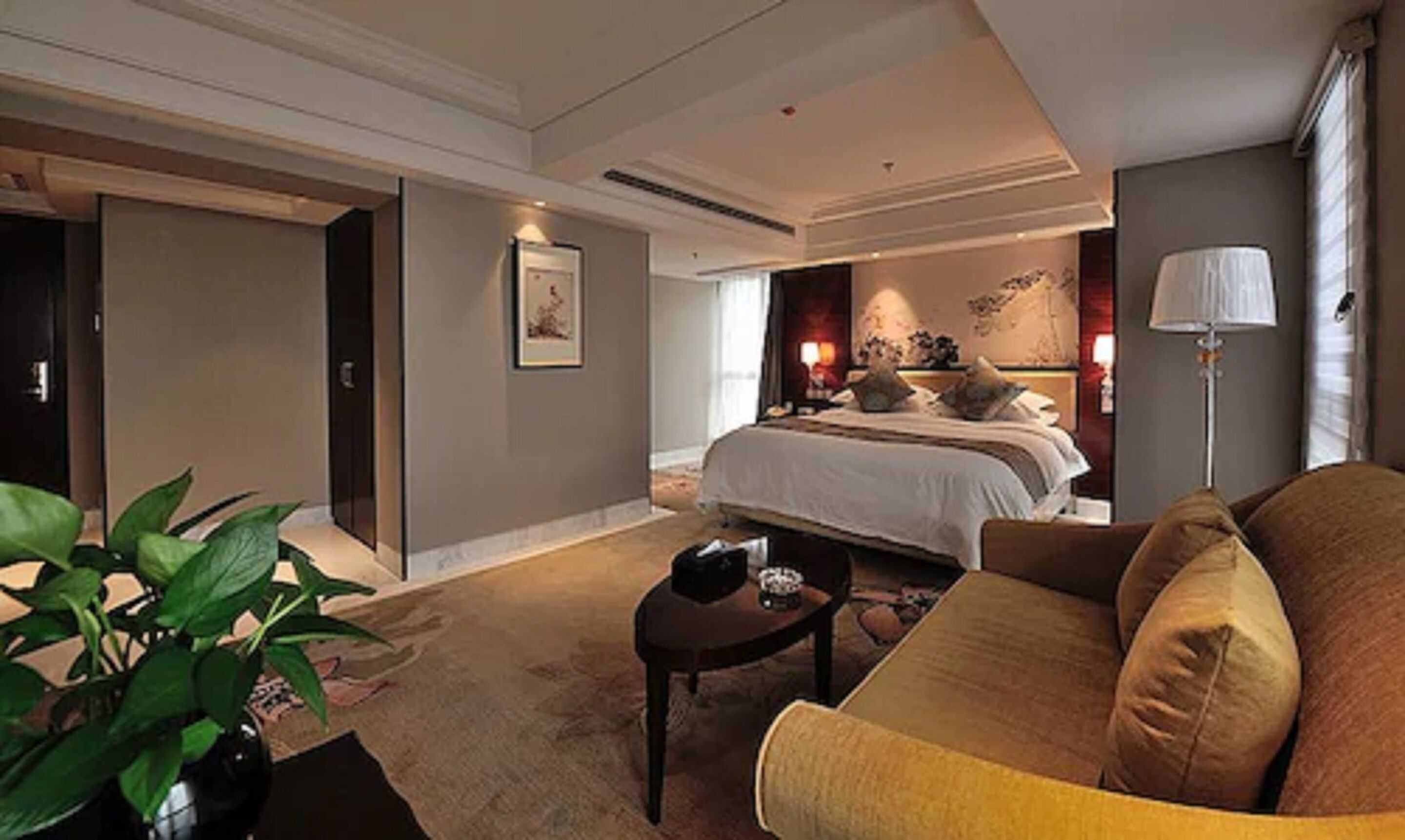 Une chambre d’hôtel avec un grand lit, un coin salon avec un canapé, une petite table et une plante en pot.