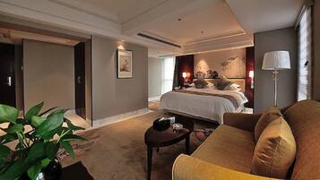 Une chambre d’hôtel avec un grand lit, un coin salon avec un canapé, une petite table et une plante en pot.