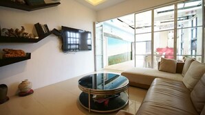 A modern living room with a sofa, a glass coffee table, and a flat-screen TV mounted on the wall.