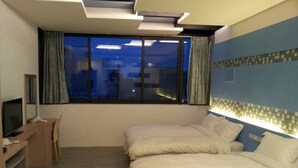 A hotel room with two beds, a desk with a television, and a window with curtains.