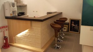 A compact kitchen with a built-in stove, a coffee maker, and a fire extinguisher. There are three stools and a framed picture on the counter.