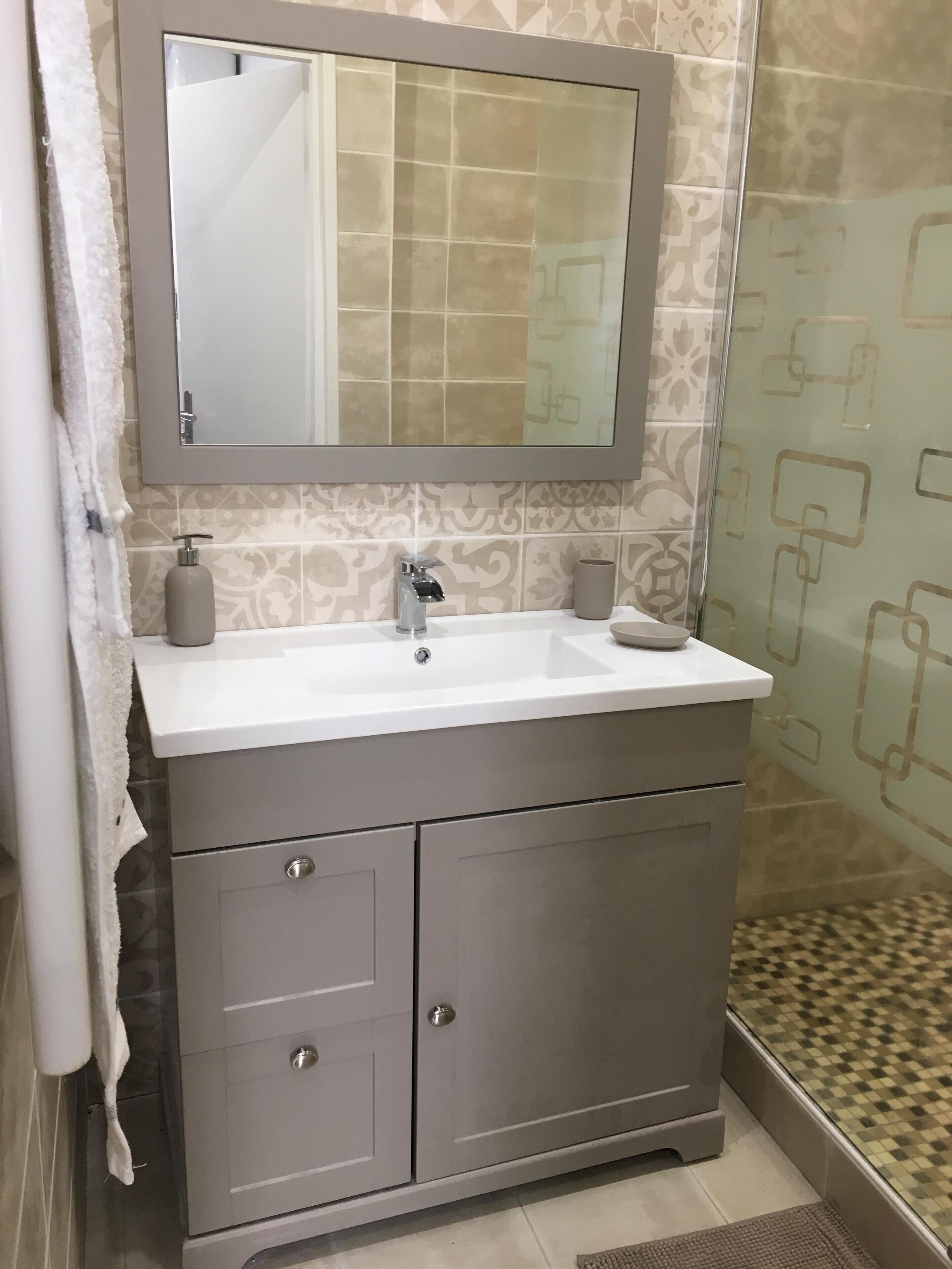 Un baño con un lavamanos blanco, un espejo encima y una pared de azulejos estampados.