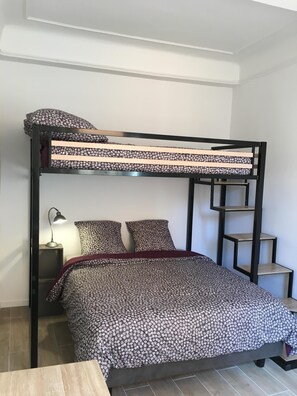 A bunk bed with a floral-patterned bedspread, a red blanket, and a nightstand with a lamp.