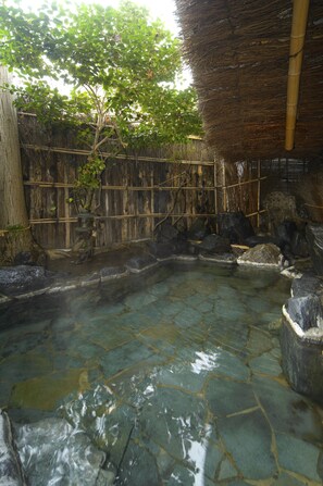 A traditional Japanese onsen with a stone bath, bamboo structures, and a thatched roof. - Tsubakikan (Aomori)