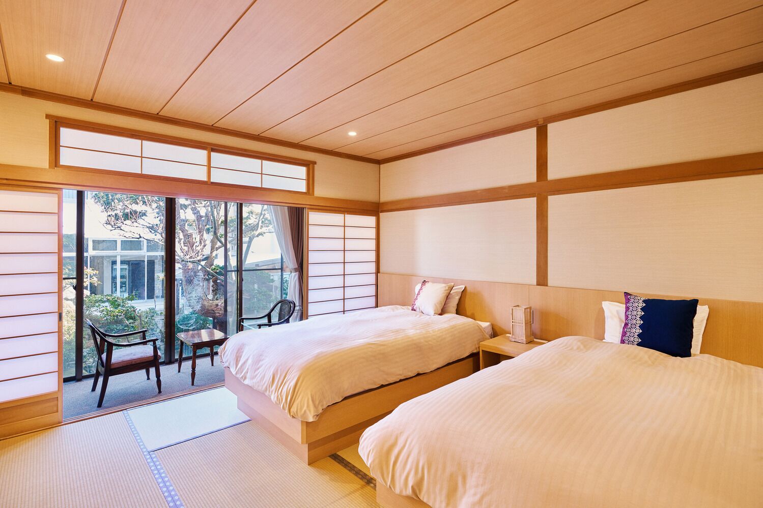 A traditional Japanese-style hotel room with tatami flooring, sliding doors, and a view of a garden.