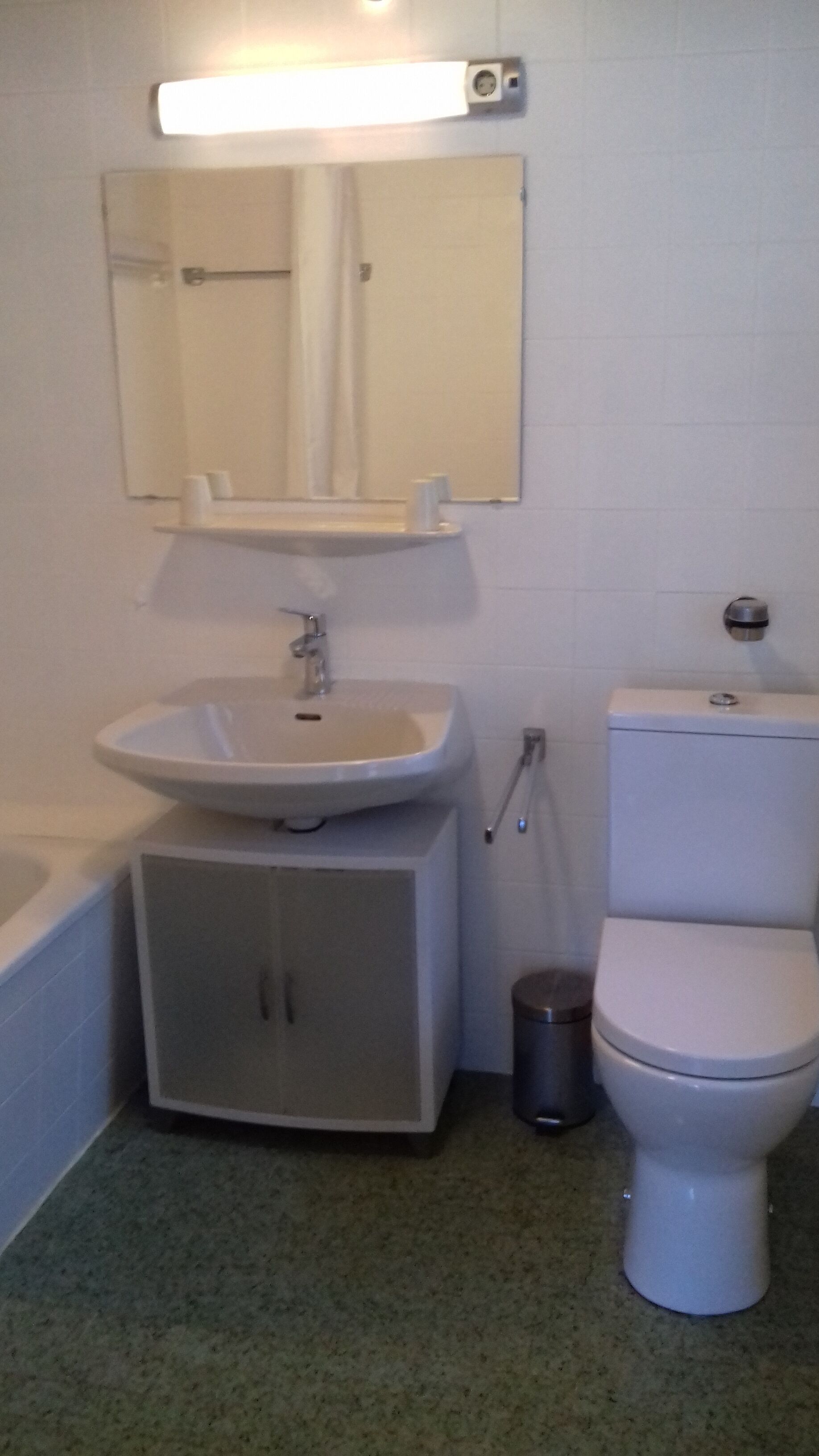 A bathroom with a sink, mirror, toilet, and a trash can.