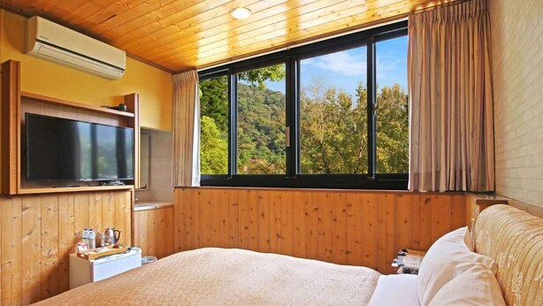 A bedroom with a large bed, a TV, a small table with bottles, and a window with curtains. - Tan Hsiang Yu B&B (Yuchi)
